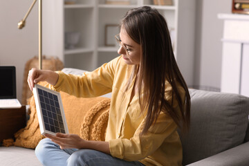 Pretty young woman with portable solar panel at home