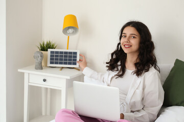 Teenage girl with laptop and portable solar panel in bedroom