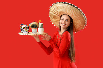 Beautiful woman in sombrero hat, with painted skull and cacti on red background. Mexico's Day of the Dead (El Dia de Muertos)