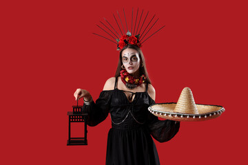 Young woman with painted skull on her face, sombrero and lantern against red background....