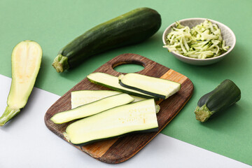 Wooden board and bowl with slices of fresh green zucchini on colorful background