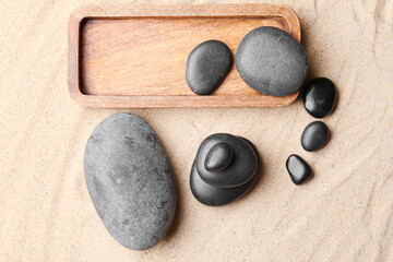 Fototapeta na wymiar Wooden tray with spa stones on sand background. Zen concept