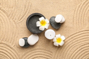 Fototapeta na wymiar Spa stones, candle and plumeria flowers on sand with lines. Zen concept