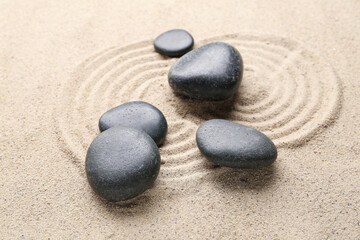 Fototapeta na wymiar Black spa stones on sand with circles, closeup. Zen concept
