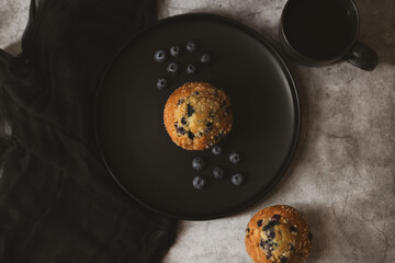 There is a cupcake and blueberries on a black plate. Breakfast concept