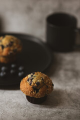 There is a cupcake and blueberries on a black plate. Breakfast concept