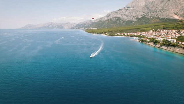 Coastal Adventures Await on Dalmatian Shoreline. A speedboat leaves a wake in the azure sea, contrasting the still mountains and sky.