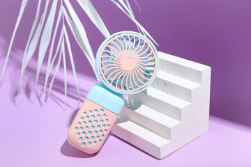 Plaster podium with portable electric fan and palm leaf on purple background, closeup