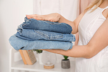 Young woman with stack of stylish jeans in wardrobe at home, closeup