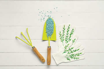 Gardening shovel with blue granular fertilizer, rake and gloves on white wooden background