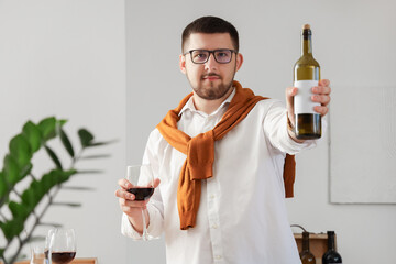 Young sommelier with bottle and glass of wine in kitchen at home