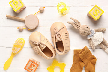 Stylish baby shoes with socks, brush and toys on white wooden background