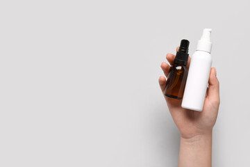 Female hand with bottles of cosmetic products on grey background, closeup