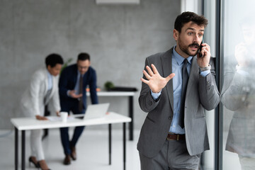 Stressed young businessman talking on mobile phone at office