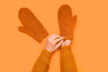 Female hands in knitted mittens on orange background