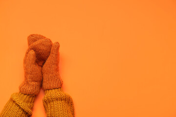 Female hands in knitted mittens on orange background
