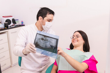 Dentist talking and explaining to his patient the treatment procedure with a dental x-ray.