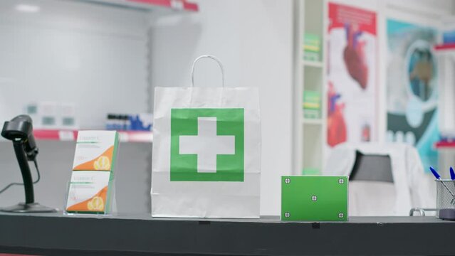 Paper bag with medicine and greenscreen surface shown on pills box at checkout counter, empty pharmacy having medicaments and vitamins at cash register. Nutrients and chromakey copyspace layout.