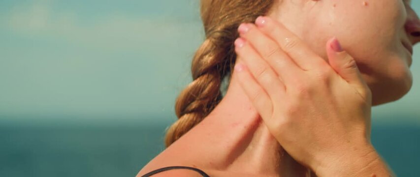 Close-up of sunscreen applying on neck. Woman using cosmetics with uv protection on beach background. Importance of protecting skin from sun