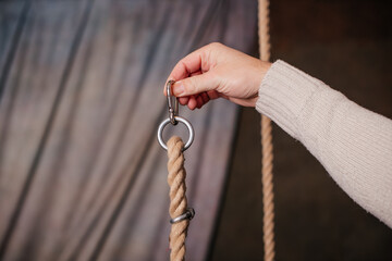 A close-up of a hand securing a rope swing with a metal loop, emphasizing durability and design.
