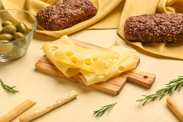 Board with tasty cheese slices, olives, rosemary and bread on beige background, closeup