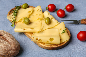 Board with tasty cheese slices, olives, tomatoes and bread on blue background, closeup