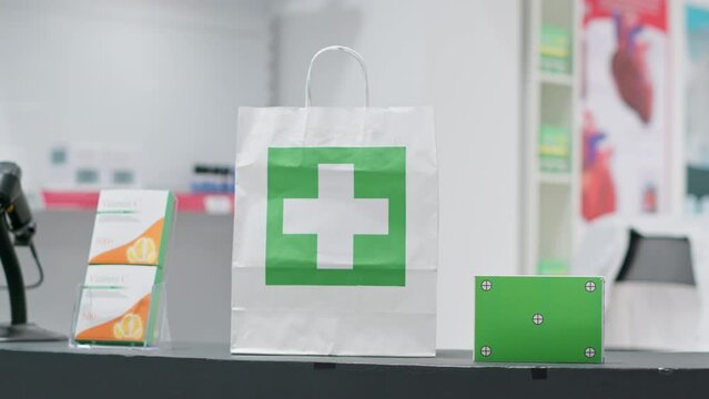 Empty pharmacy with pills and vitamins at cash register, paper bag containing pharmaceuticals alongside greenscreen layer on pill box at checkout area. Chromakey copyspace design next to purchase.