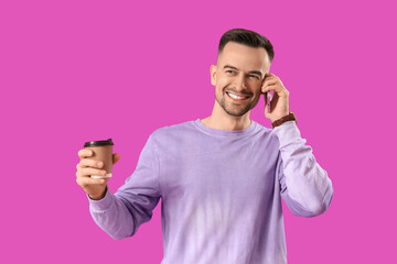 Happy young man with cup of coffee talking by mobile phone on purple background