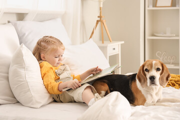 Naklejka premium Cute little girl with book and Beagle dog in bedroom
