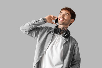 Happy young man with headphones talking by mobile phone on grey background