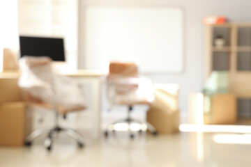 Blurred view of office with chairs wrapped in stretch film and cardboard boxes on moving day