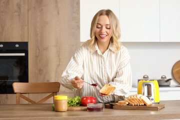 Young beautiful happy woman making tasty toasts with jam in kitchen