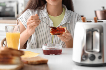 Young beautiful woman drinking orange juice and eating tasty toast with jam in kitchen, closeup