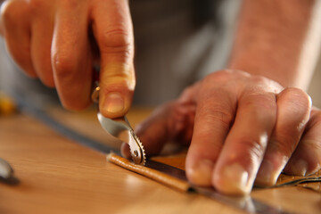 Man marking leather with roller in workshop, closeup