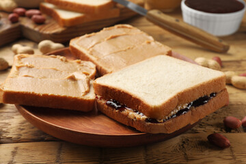 Tasty peanut butter sandwiches with jam and peanuts on wooden table, closeup