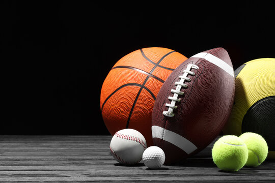 Many different sport balls on dark wooden table against black background, space for text