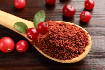 Dried cranberry powder in spoon, fresh berries and green leaves on wooden table, closeup