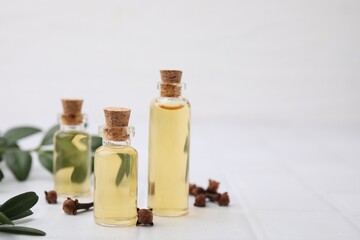 Clove oil in bottles, leaves and dried buds on white tiled table, closeup. Space for text