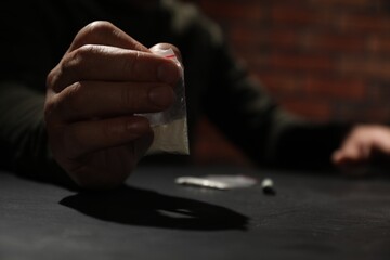 Drug addiction. Man with plastic bag of cocaine at grey table, selective focus - obrazy, fototapety, plakaty