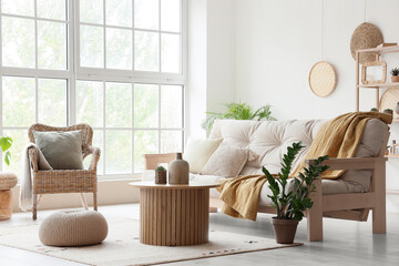 Interior of light living room with cozy white sofa, coffee table and wicker armchair