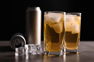 Energy drink in glasses, aluminium cans and ice cubes on grey table