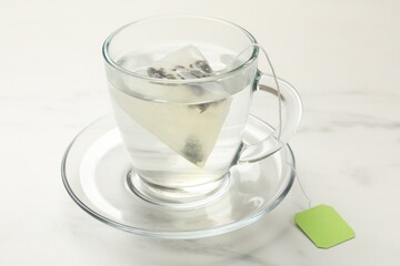 Tea bag in glass cup on white table, closeup