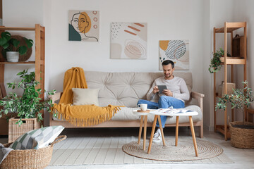 Handsome man with tablet computer resting on white sofa in modern living room