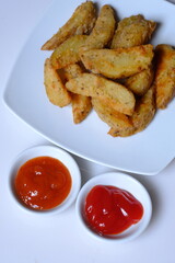 Potato wedges are irregular wedge-shaped slices of potatoes, often large and unpeeled, that are baked or fried. served on a plate. tomato sauce and chili sauce.