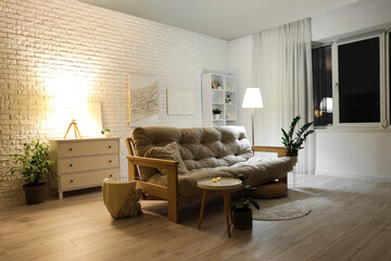 Interior of modern living room with white sofa and glowing lamps at evening