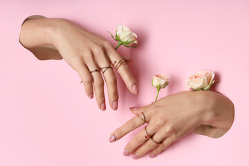 Female hands with rings and roses visible through holes in pink paper