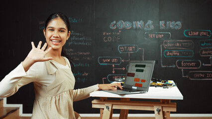 Smart highschool girl waving to camera while programing code at blackboard with engineering code or...