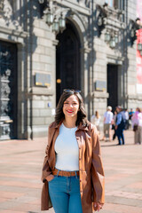 Happy young mexican woman in embroidered top looking at screen of smartphone while standing in front of blurred Munal museum in downtown Mexico City and browsing pictures in daylight