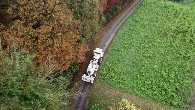 High Resolution Video of a Vibro-Truck shot with a drone. It shows the truck driving on a dirt road, while the drone flies above it, following its path.