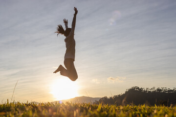 Silhouette happy young girl jumping on mountain beautiful sunset sky background.